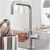 Felhasználó használja a Grohe Blue Home konyhai csaptelepet, szűrt vizet önt a vízforralóba az U-alakú kifolyócsőből, kiemelve a könnyű használhatóságot.