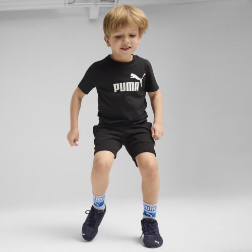 Fiatal fiú fekete Puma ESS No. 1 Logo Tee PS pólóban és rövidnadrágban, boldogan ugrik, kék-fehér zokniban és sötétkék sportcipőben - Baba és gyerek divat