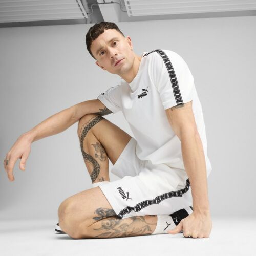 Fiatal tetovált férfi Puma ESS TAPE Tee férfi fehér pólóban és fehér rövidnadrágban, guggoló pózban, életkép 