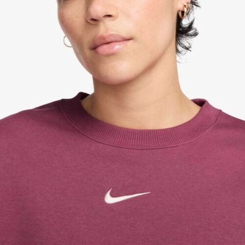 Részletes közeli felvétel a fehér Nike Swoosh logóról a mély lila Nike W NSW PHNX FLC OOS CREW pulóveren, kiemelve a minőséget és az anyag textúráját. - Női melegítő