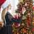 Woman decorating a Springos 250 cm artificial Christmas tree, Caucasian spruce, with ornaments and lights