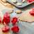 Red plastic cookie cutters with spring-loaded plungers, shown in use on a baking sheet and a silicone baking mat