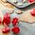 Red plastic cookie cutters with spring-loaded plungers, shown in use on a baking sheet and a silicone baking mat