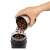 DeLonghi KG-200 coffee grinder, black, hand pouring coffee beans into the grinder