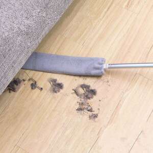 Long-handled crevice cleaner being used to clean under a couch, removing dust and debris - Cleaning brush