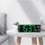 Digital wall clock with green LED display showing time, date, day of the week, and temperature, placed on a table