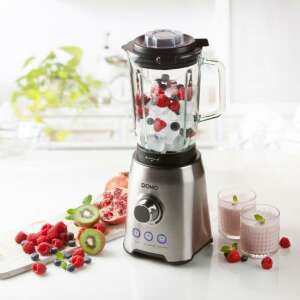 Domo DO710BL turmixgép üvegkancsóval, jéggel, eperrel és áfonyával töltve, fehér munkalapon gyümölcsökkel és két pohár smoothie-val - Domo