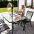 Springos garden table with tempered glass top and black metal frame, with a beige parasol and chairs