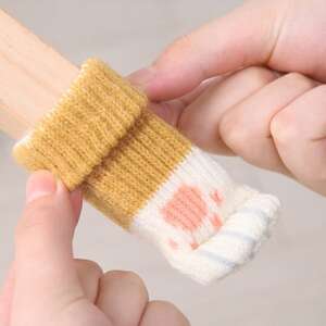 Kéz tart egy sárga és fehér csíkos cica mancsos székláb védőt, bútorláb védőt, padlóvédőt egy fa széklábon - Padlóvédő bútorláb alátét