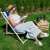Woman relaxing in a Springos blue and white striped wooden deck chair in a garden