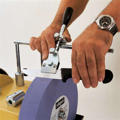 Scheppach jig for sharpening knives, a person is using the jig to sharpen a knife on a grinding wheel