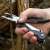 Hand holding True Utility Fireranger multitool, black and silver, using the pliers to cut a branch