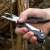 Hand holding True Utility Fireranger multitool, black and silver, using the pliers to cut a branch