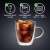 Bialetti Capri double-walled glass mug with handle, filled with iced coffee, with icons showing it is made of borosilicate glass, dishwasher safe, and microwave safe