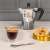 Bialetti Firenze 80ml double-walled glass espresso cup, filled with coffee, on a table with cookies and a coffee maker