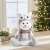 Sitting snowman Christmas decoration with an owl hat, 30 x 20 x 14 cm, on a table with a Christmas tree in the background