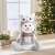Sitting snowman Christmas decoration with an owl hat, 30 x 20 x 14 cm, on a table with a Christmas tree in the background