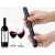 Hand holding a black pneumatic wine opener, with a bottle of wine and two glasses of wine in the background