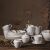 Teljes Ambition Perla New Bone China étkészlet tányérokkal, tálakkal, bögrékkel, tejszínes kiöntővel és cukortartóval egy rusztikus asztalon.
