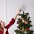 Woman placing silver star Christmas tree topper on tree