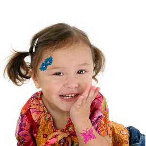 Lány csillámtetoválással az arcán és a karján, bemutatva a csillámtetováló készlet szórakoztató és kreatív lehetőségeit - Tetoválás